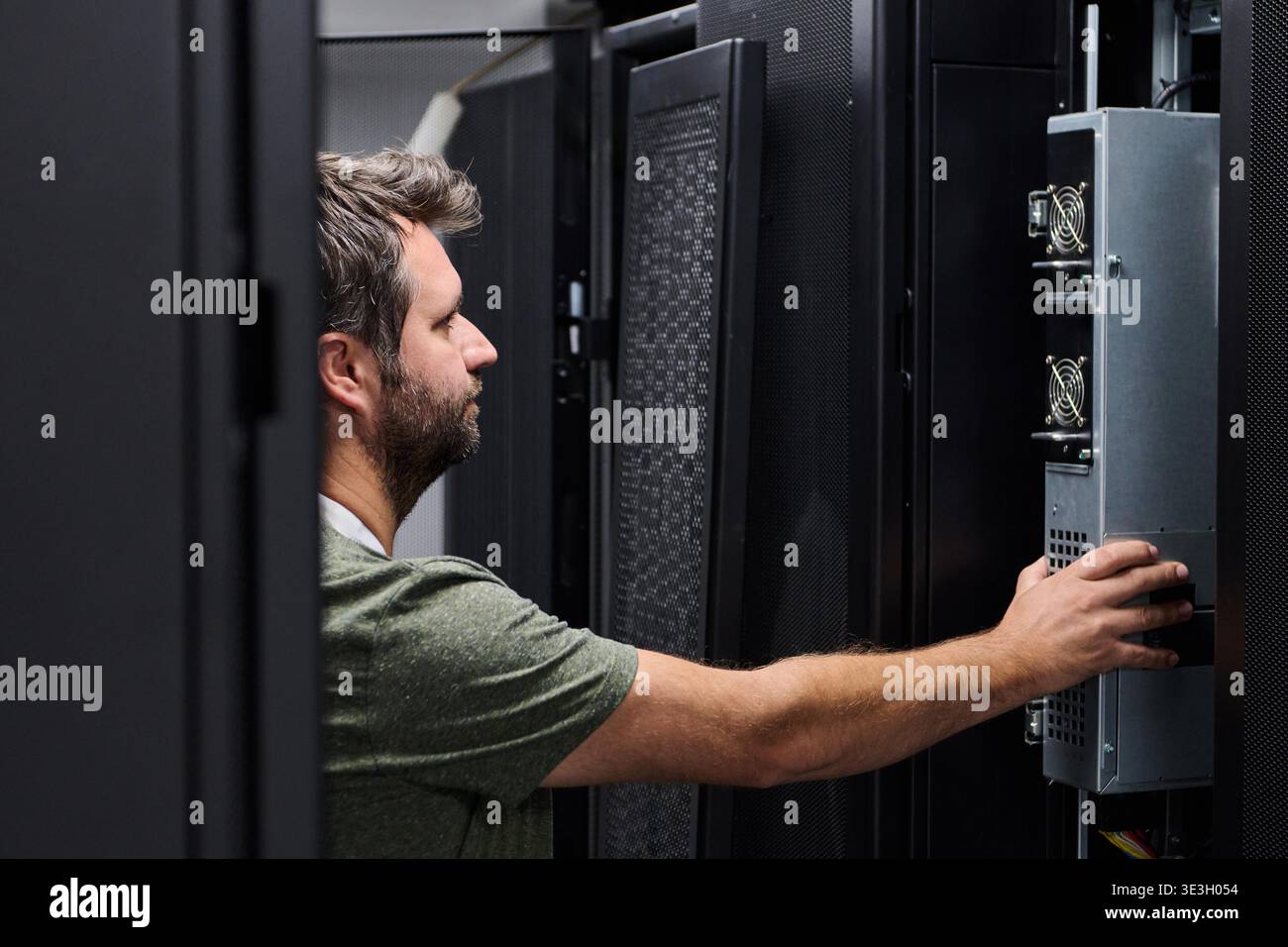 Focused IT technician working inside a data center, installing and inspecting server hardware in a rack for maintenance and system reliability. || Model released Stock Photo
