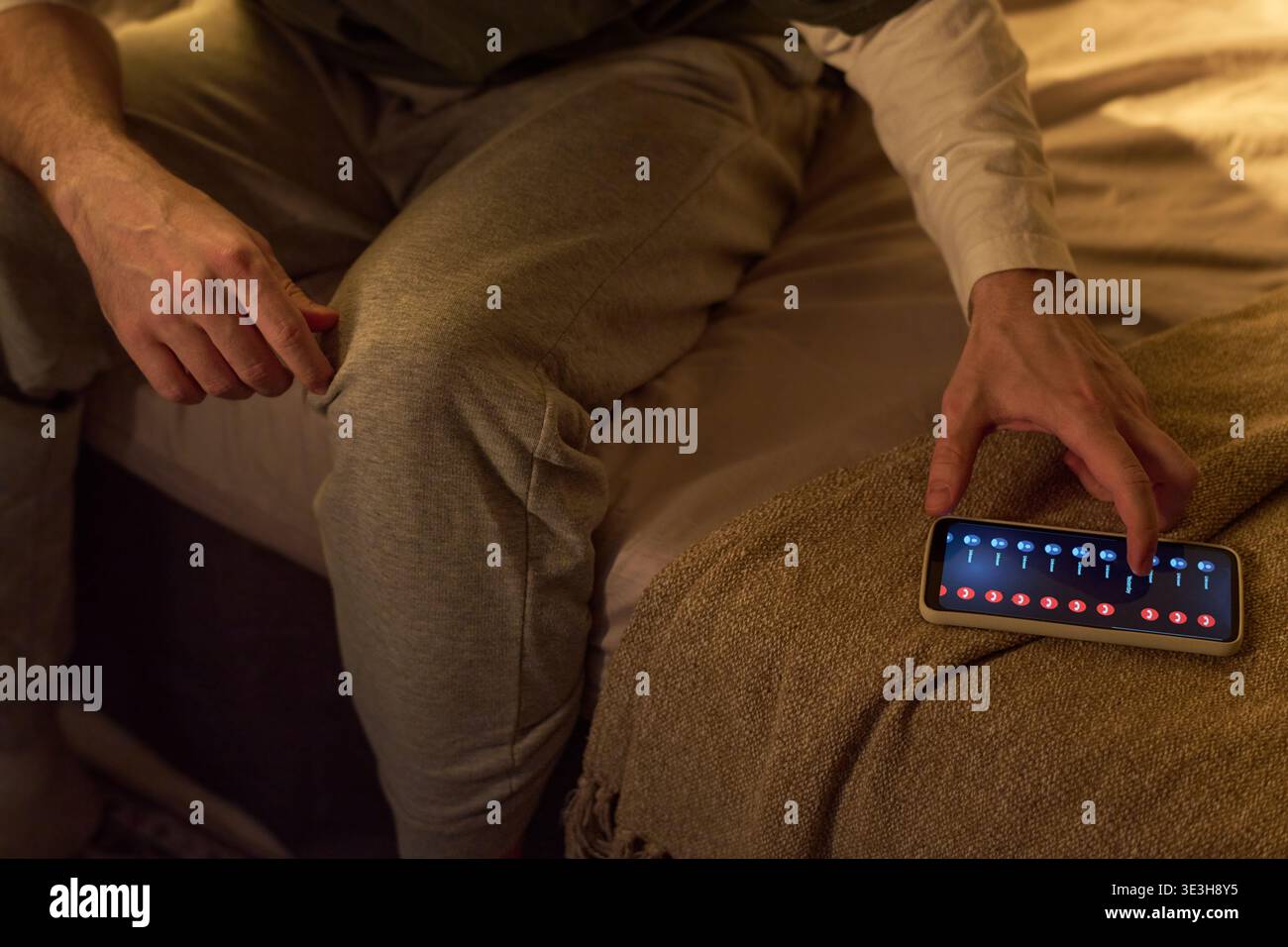 Young Man Using Smartphone to Control Smart Home Lighting Stock Photo