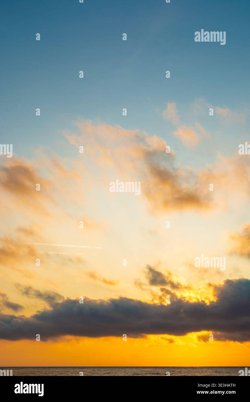 changing weather forecast. air pressure. scenic cloudscape. golden clouds on the blue morning sky over sea horizon. idyllic sunrise vertical backgroun Stock Photo