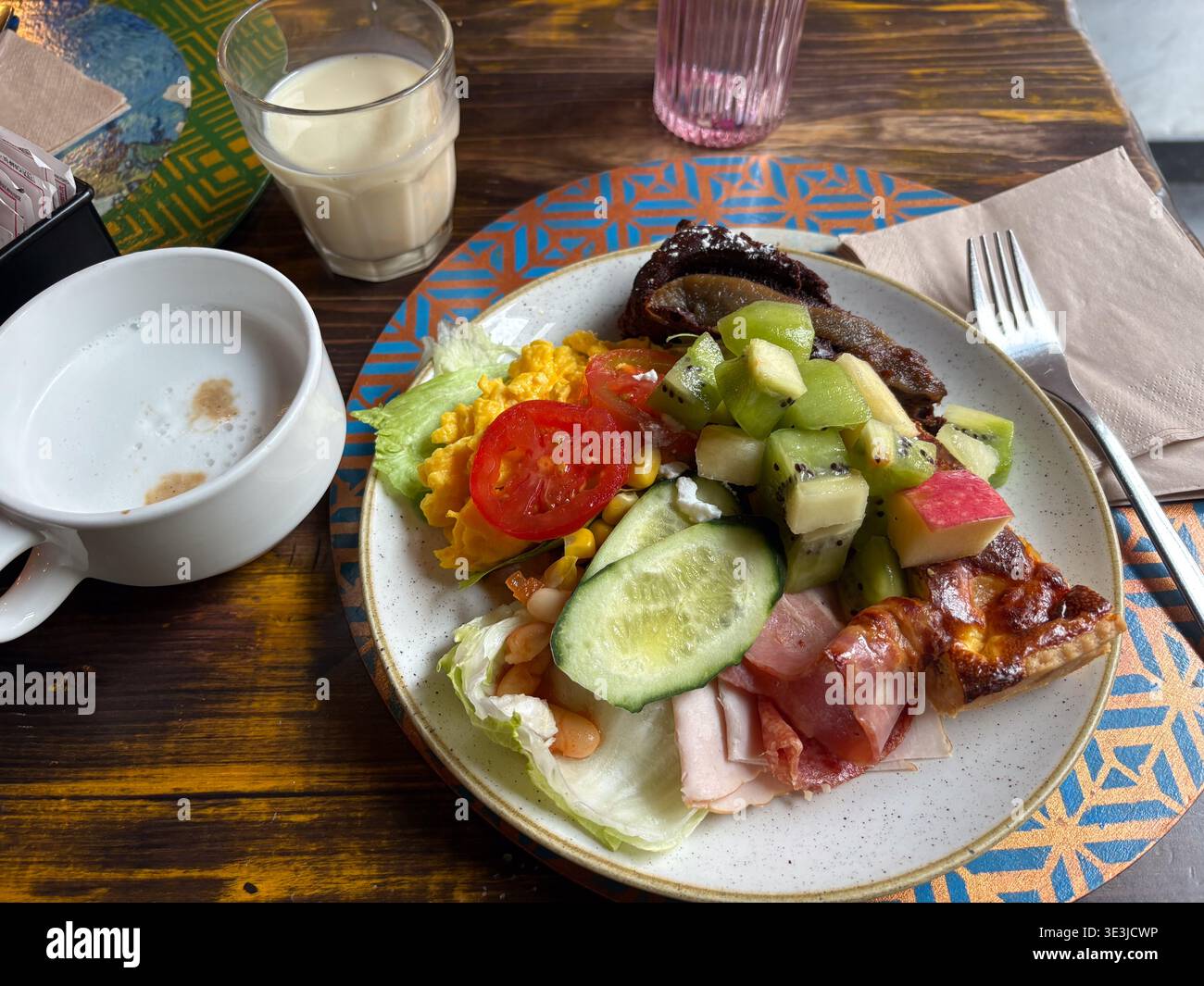 Hotel buffet breakfast in Rome, Italy. Plate with kiwi, scrambled eggs, cold cuts, and quiche served on patterned placemat. Stock Photo