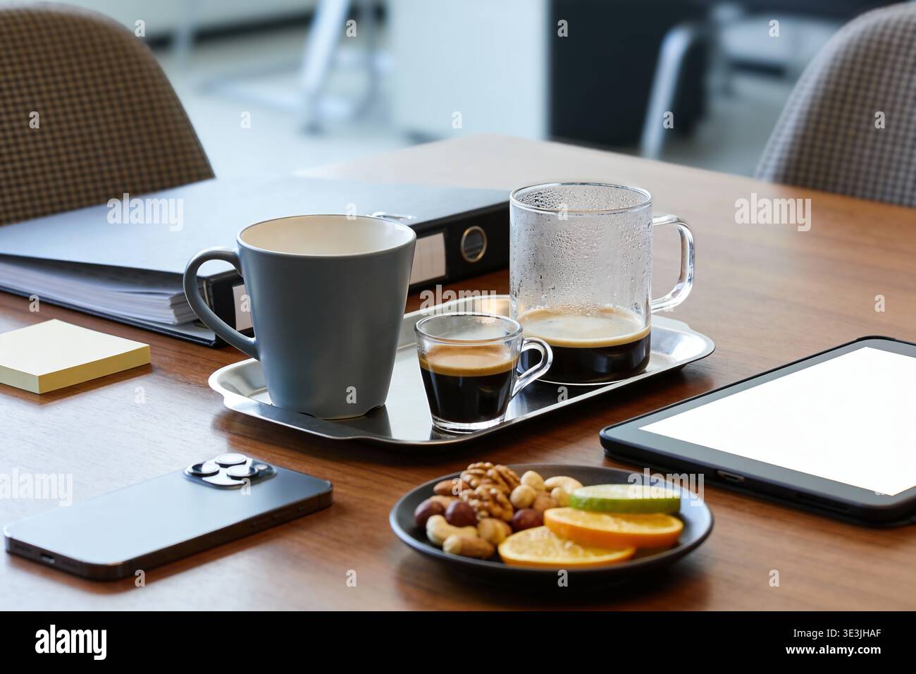 A modern office desk setup featuring coffee cups, a mix of nuts and citrus slices, a smartphone, and a tablet, perfect for a business break Stock Photo