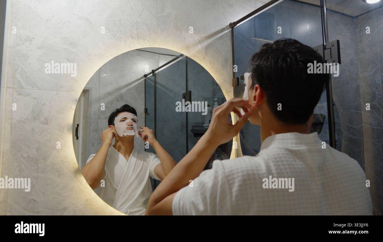 Young man applying face cream while looking in bathroom mirror Stock Photo
