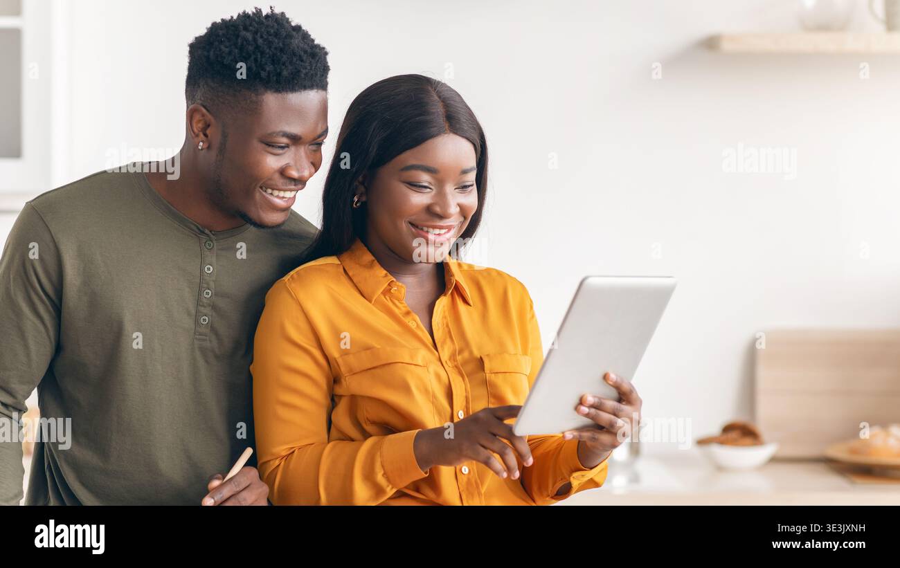 Happy Black Spouses Using Digital Tablet While Cooking Lunch In Kitchen Together Stock Photo