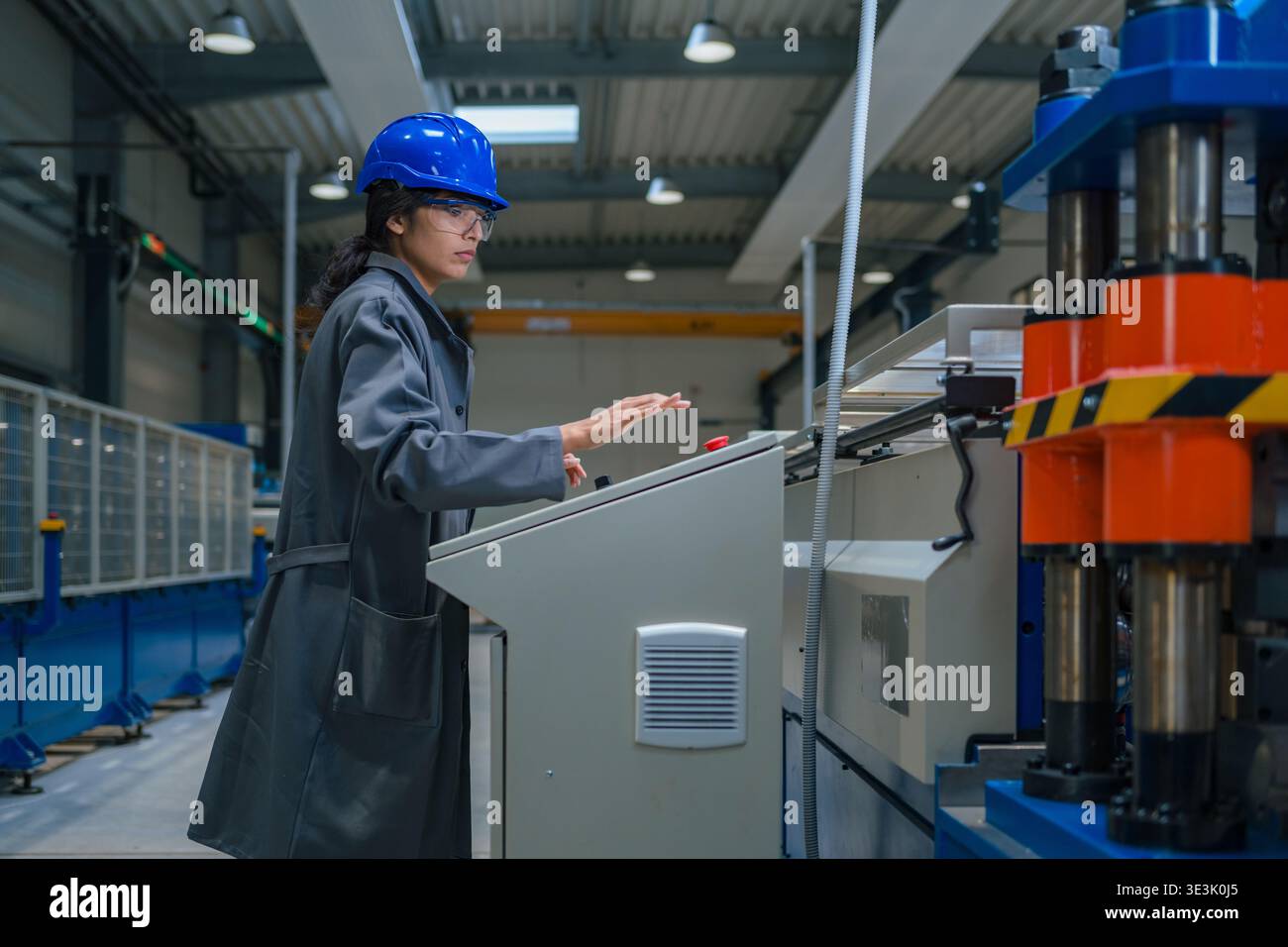 An Indian female engineer works in a factory while wearing safety gear and operating machinery. Stock Photo
