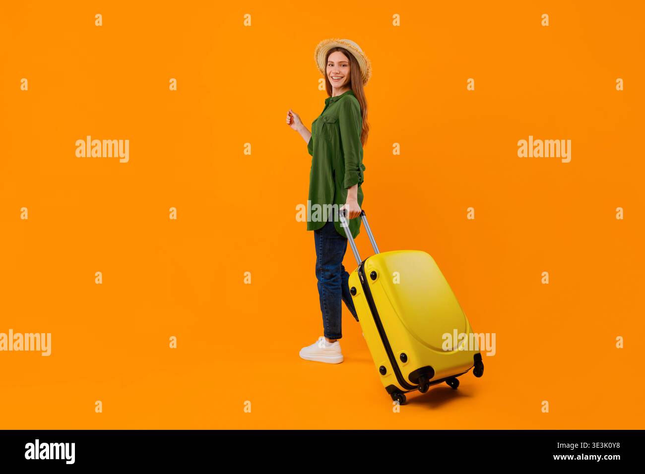 Woman With Suitcase Stands Against Bright Orange Background While Smiling Stock Photo