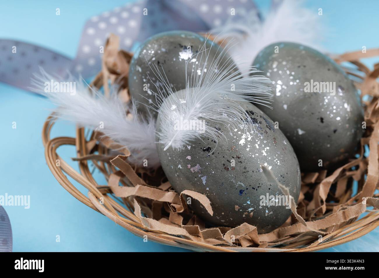 Close up Easter eggs with feathers in nest on blue background Stock Photo