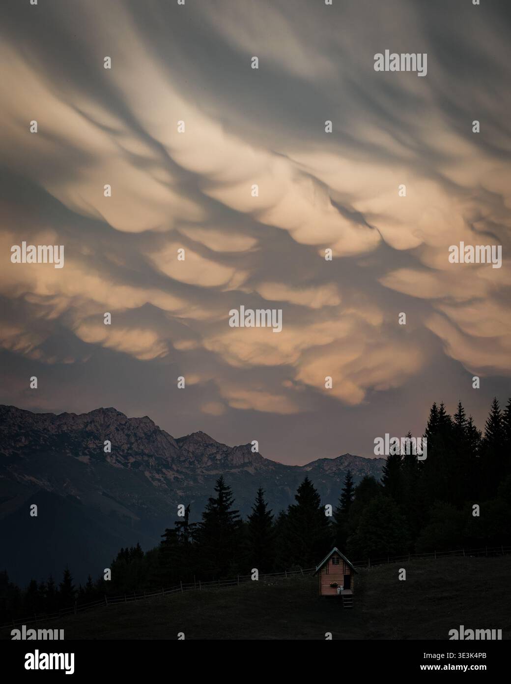 A small cabin in the mountains beneath dramatic mammatus clouds during sunset. Stock Photo