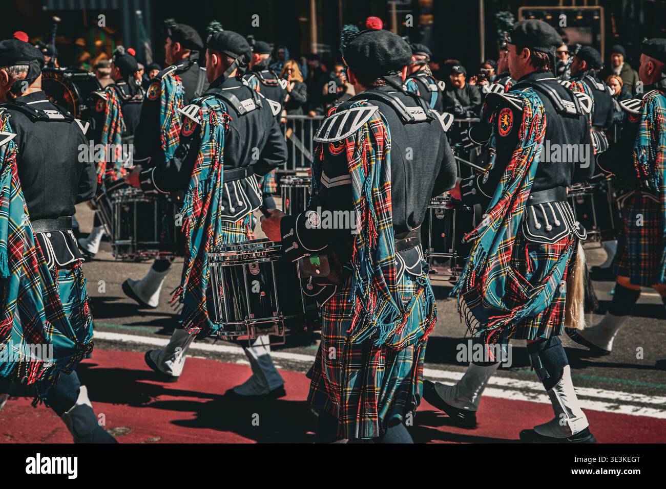 To Tbe Rear March NY MARCH 17, 2026: Rear view of a pipe band marching in bright tartan ...