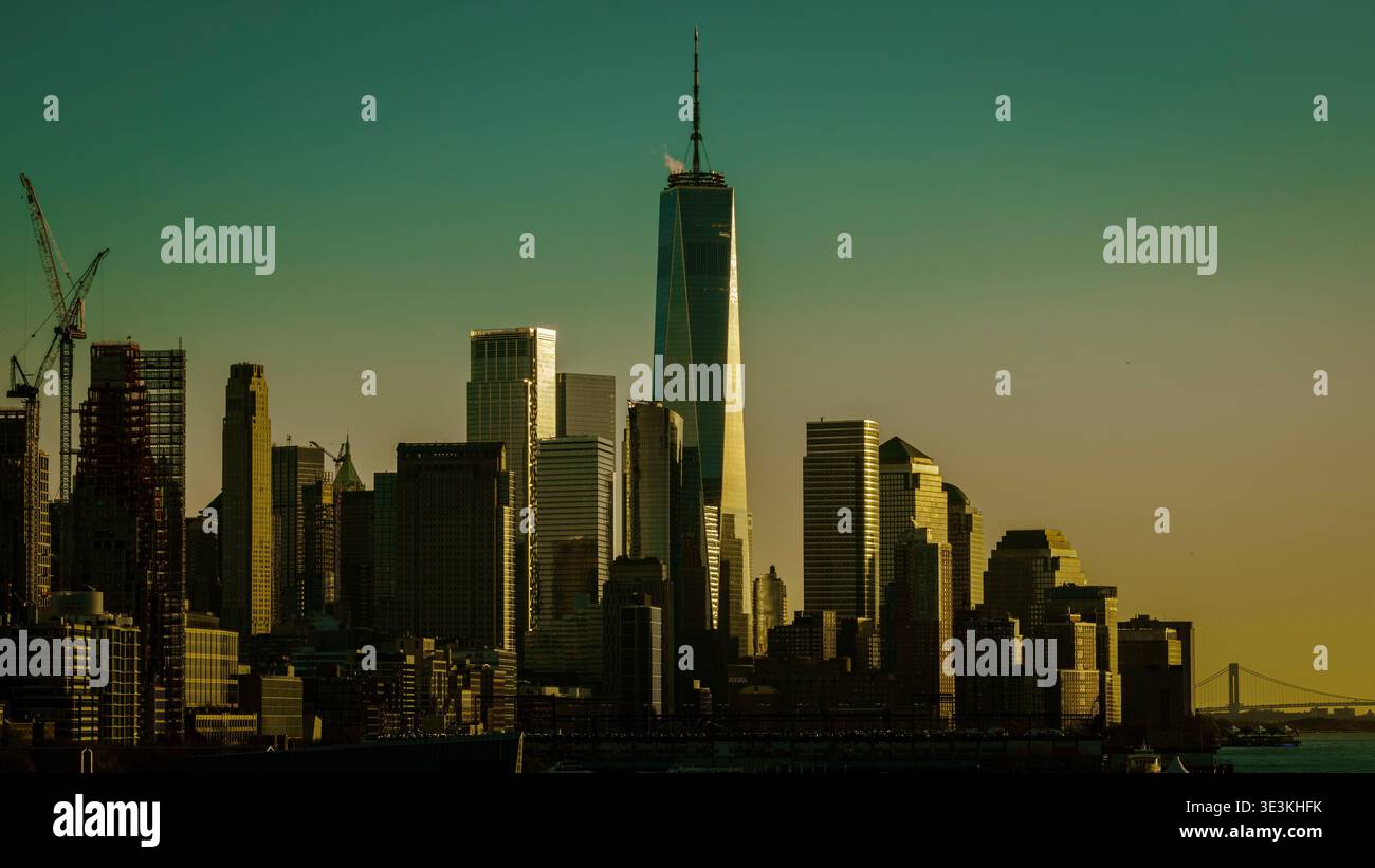 Golden hour view of the New York City skyline featuring One World Trade Center illuminated by warm sunlight, capturing the modern architecture of Lowe Stock Photo