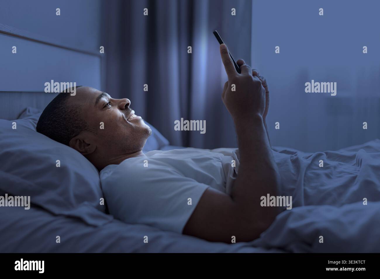 Young black man lying in bed at night using smartphone Stock Photo