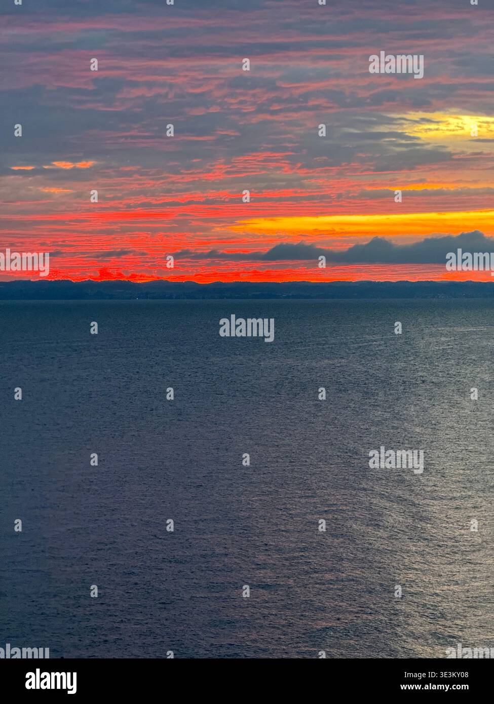 Dramatic red sunset over Lake Constance (Bodensee) with glowing clouds and calm water, tranquil evening seascape in Central Europe. - Smartphone Captured Stock Image