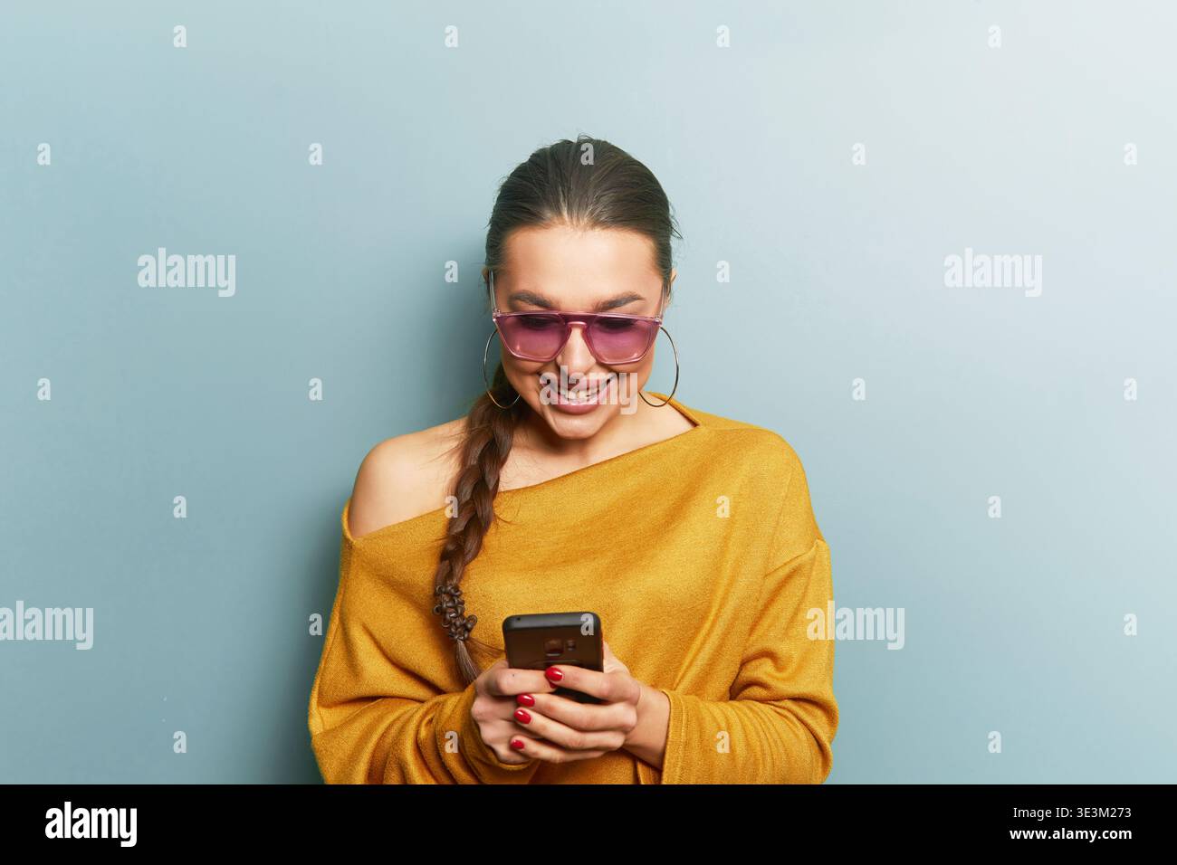 Digital lifestyle concept. Young woman holding smartphone. Smiling while texting. Casual outfit with sunglasses. Portrait focusing on face and interac Stock Photo