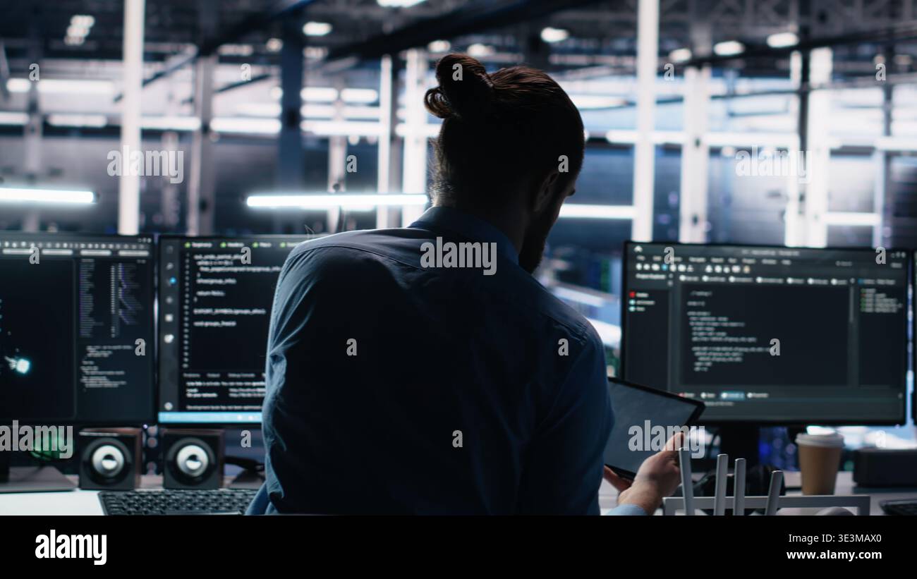 Admin using devices in data center, coding with generative AI assistance. IT employee oversees leveraging artificial intelligence large language model tech on PC, laptop and tablet, camera A Stock Photo