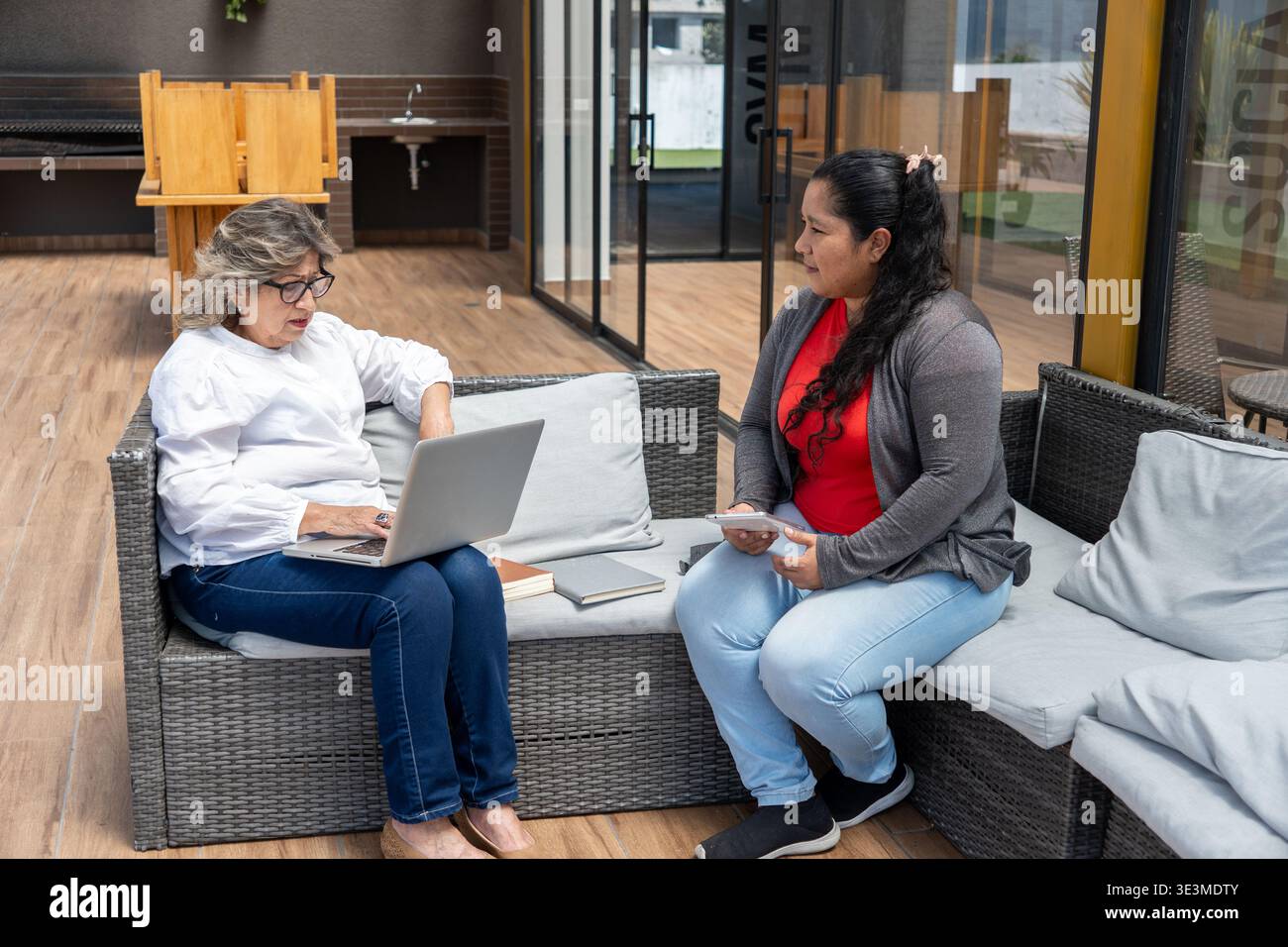 Two women relaxing on outdoor sofa, having a conversation and working on a laptop Stock Photo