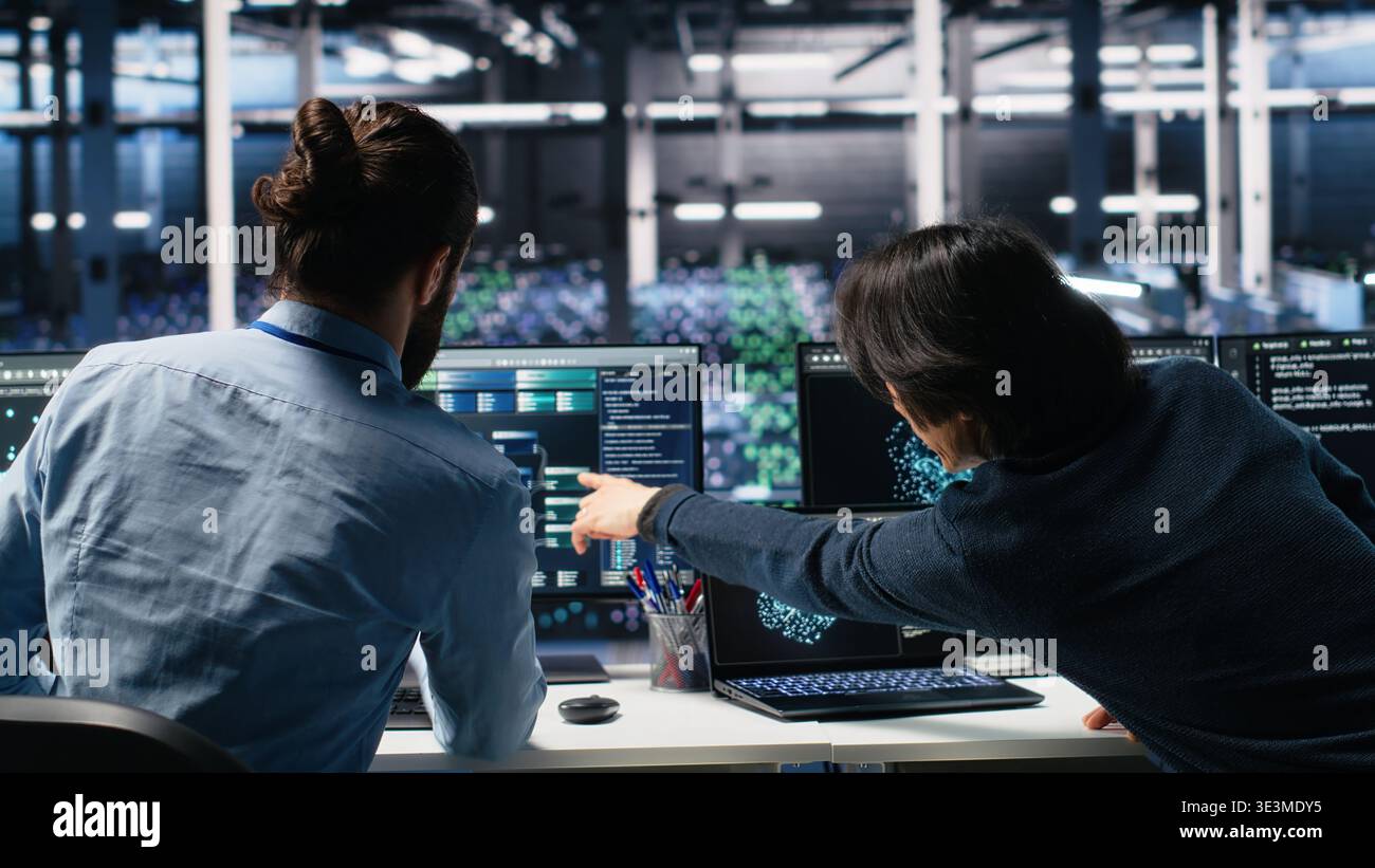 Data center admins doing brainstorming, working on neural network software development. Server farm IT employees working together, implementing machine learning technology using PC, camera A Stock Photo