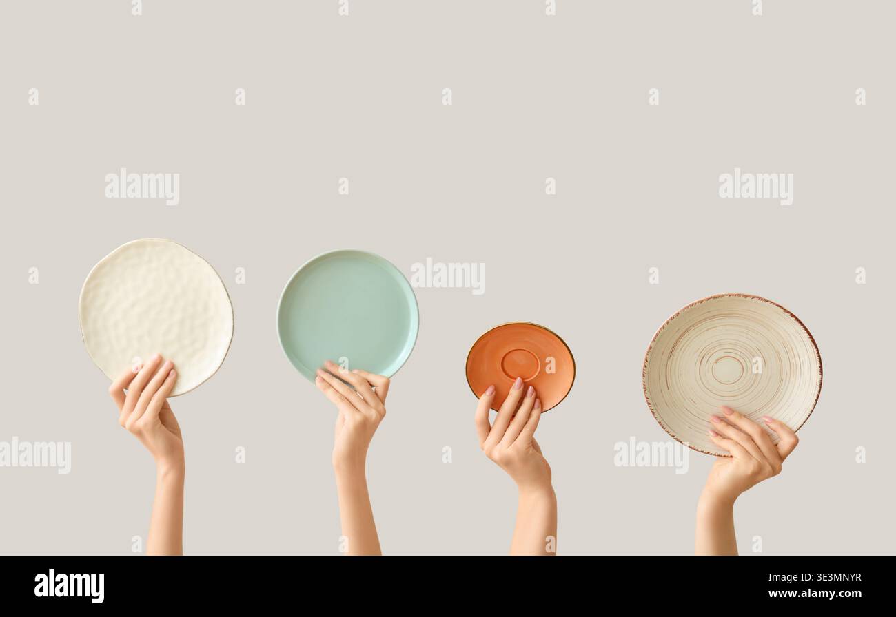 Hands holding empty plates on light background Stock Photo