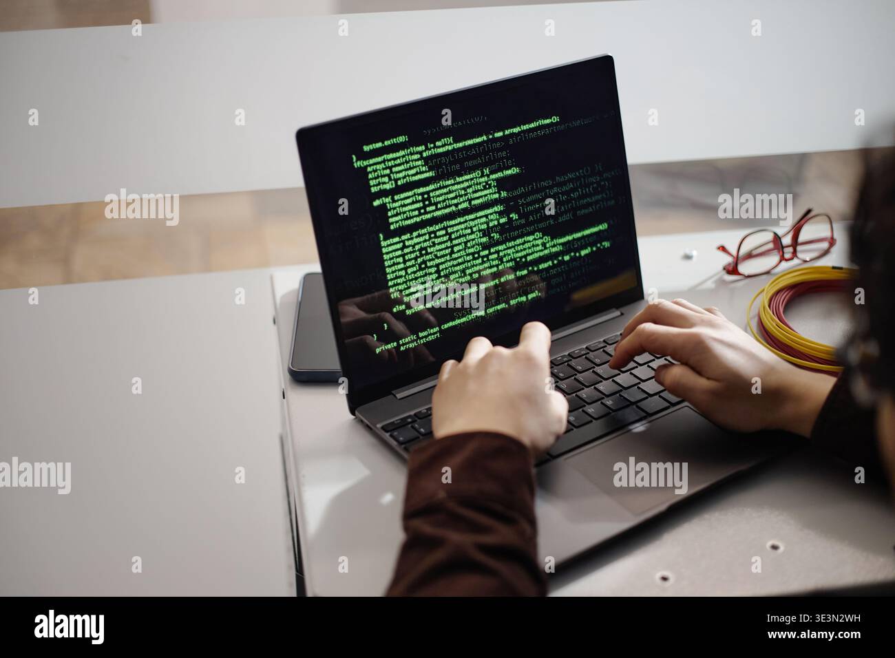 Young Adult Man Typing Code on Laptop Computer in Office Setting Stock Photo