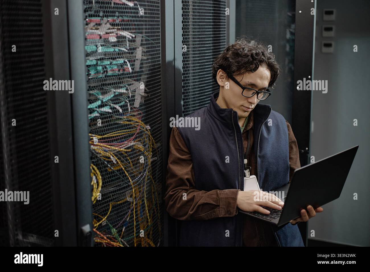 Young Adult Asian Man Using Laptop While Working Inside Server Room Stock Photo
