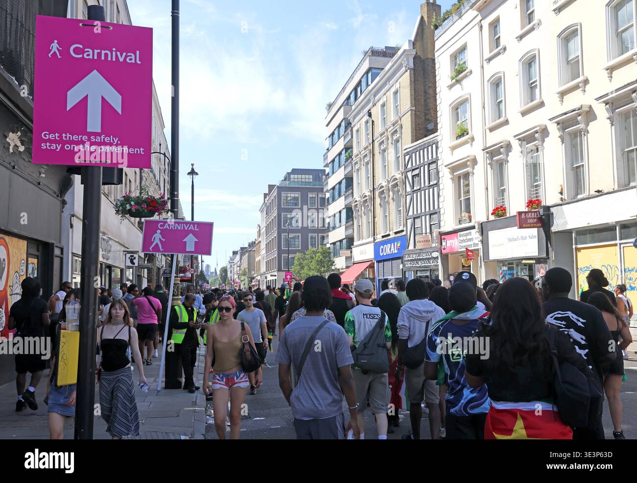 Crowds follow pedestrian pink safety signs on Westbourne Grove during Notting Hill Carnival in west London, England, UK. Get their safe to the party Stock Photo