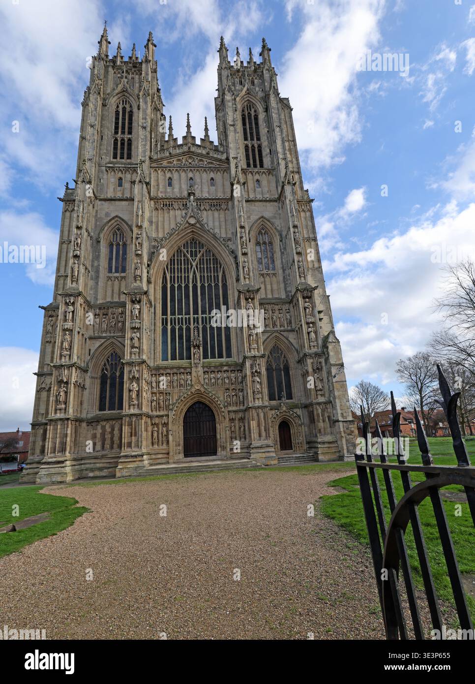 Beverley Minster Church in Beverley, East Yorkshire, viewed through open iron gates, showing the grand Gothic west front under a bright sky. Stock Photo