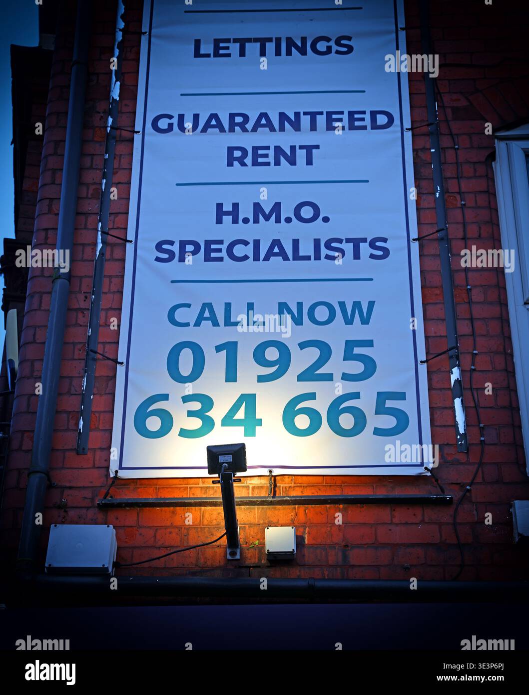 Illuminated lettings and HMO specialists sign on a brick building in Warrington, Cheshire, England, advertising guaranteed rent services. Stock Photo