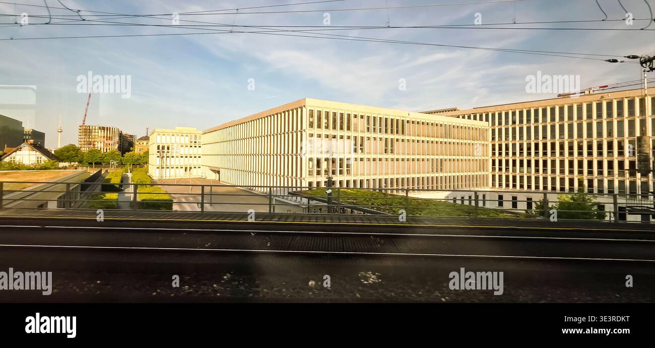 Berlin, Germany - June 13, 2025: Modern office structures are surrounded by greenery near railway tracks in urban environment. - Smartphone Captured Stock Image