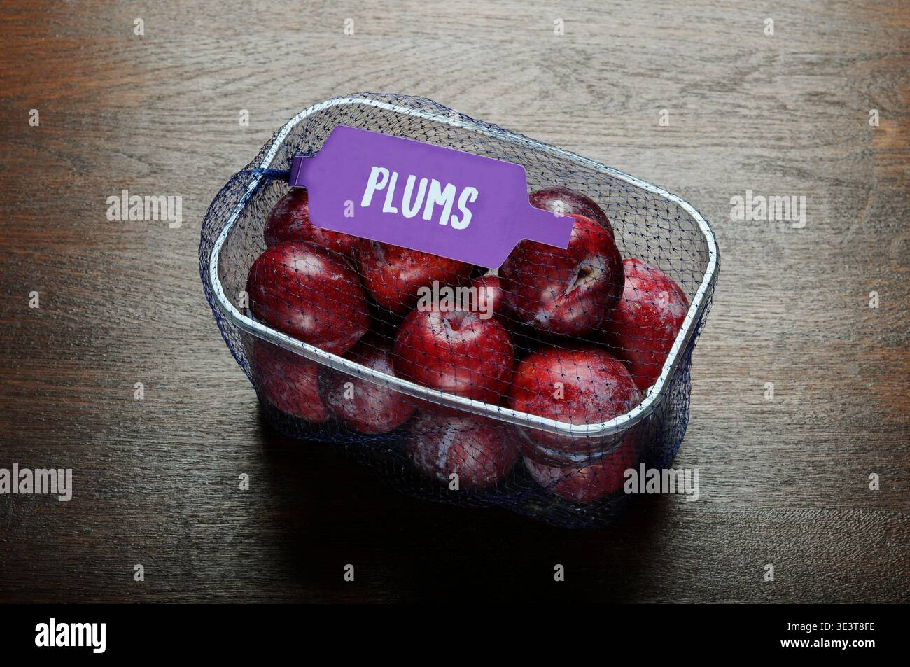 Punnet of fresh plums fruit retail container with label close up on wooden table top with copy space Stock Photo