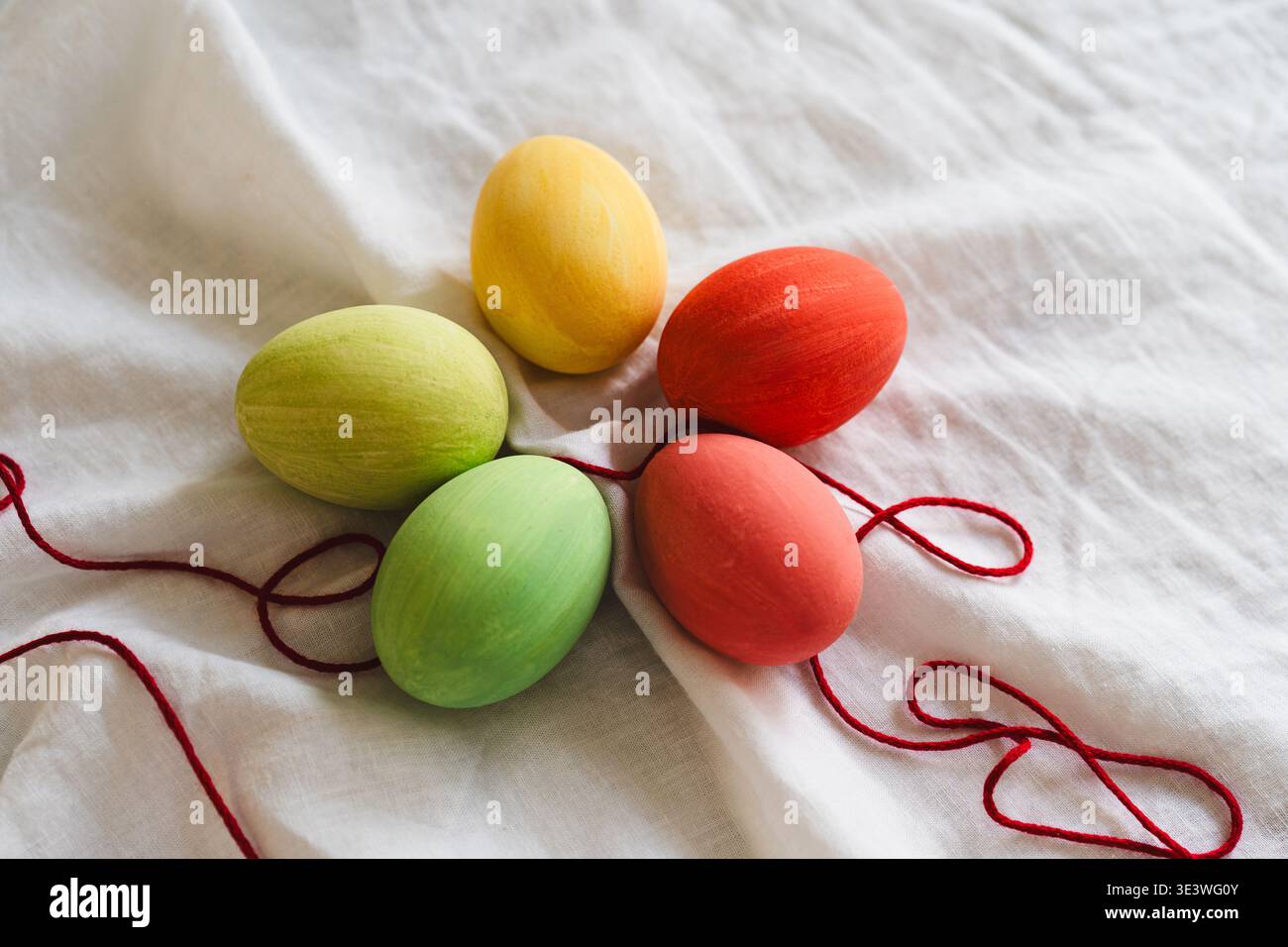 A vibrant display of multicolored Easter eggs on a soft white fabric, adorned with red string. This festive arrangement captures the joy and color of Stock Photo