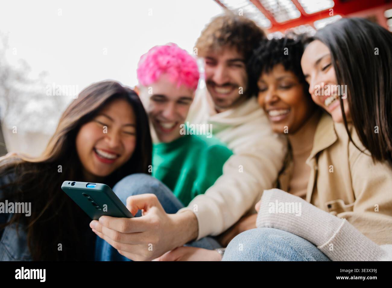 Diverse group of students sitting on campus stairs using phones together Stock Photo