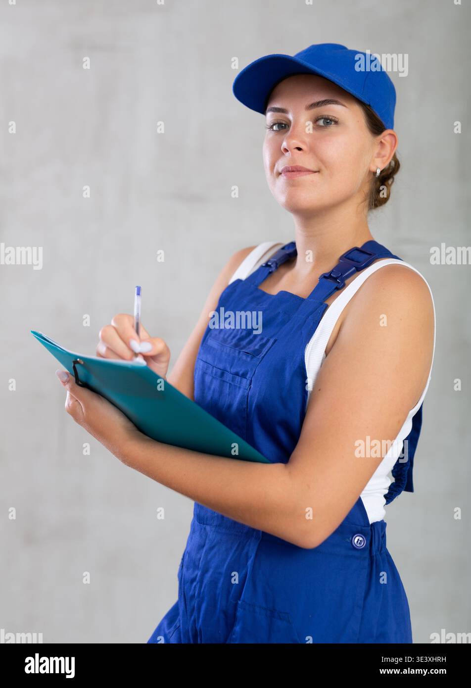 Young woman in work overalls making notes Stock Photo