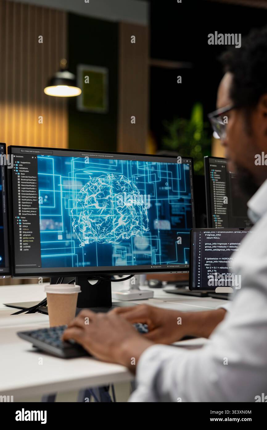 Engineer utilizing AI on computer to optimize performance and forecast issues. African american worker in tech company office training machine learning models to perform automatic updates Stock Photo