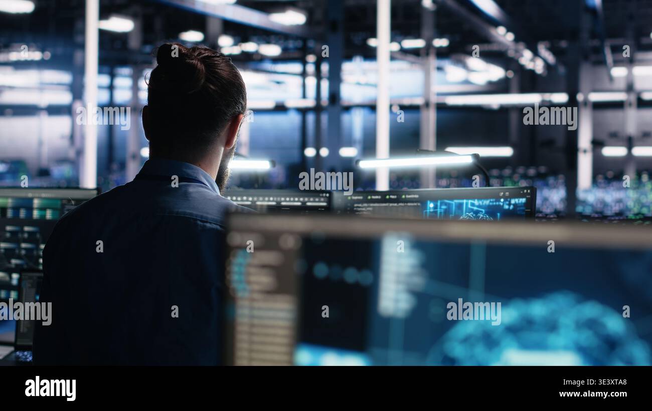 Server room software developer using AI to review infrastructure diagnostics. IT employee in data center analyzing performance data using artificial intelligence technology on devices, camera A Stock Photo