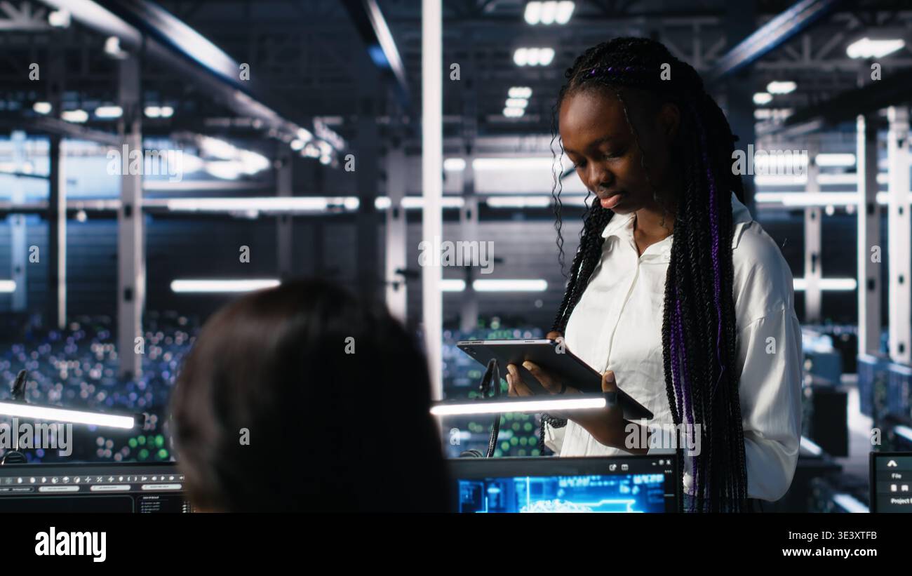 Technicians in high tech data center cooperate on neural network software development. Server hub IT workers talking, implementing deep learning technology using PC, camera A Stock Photo