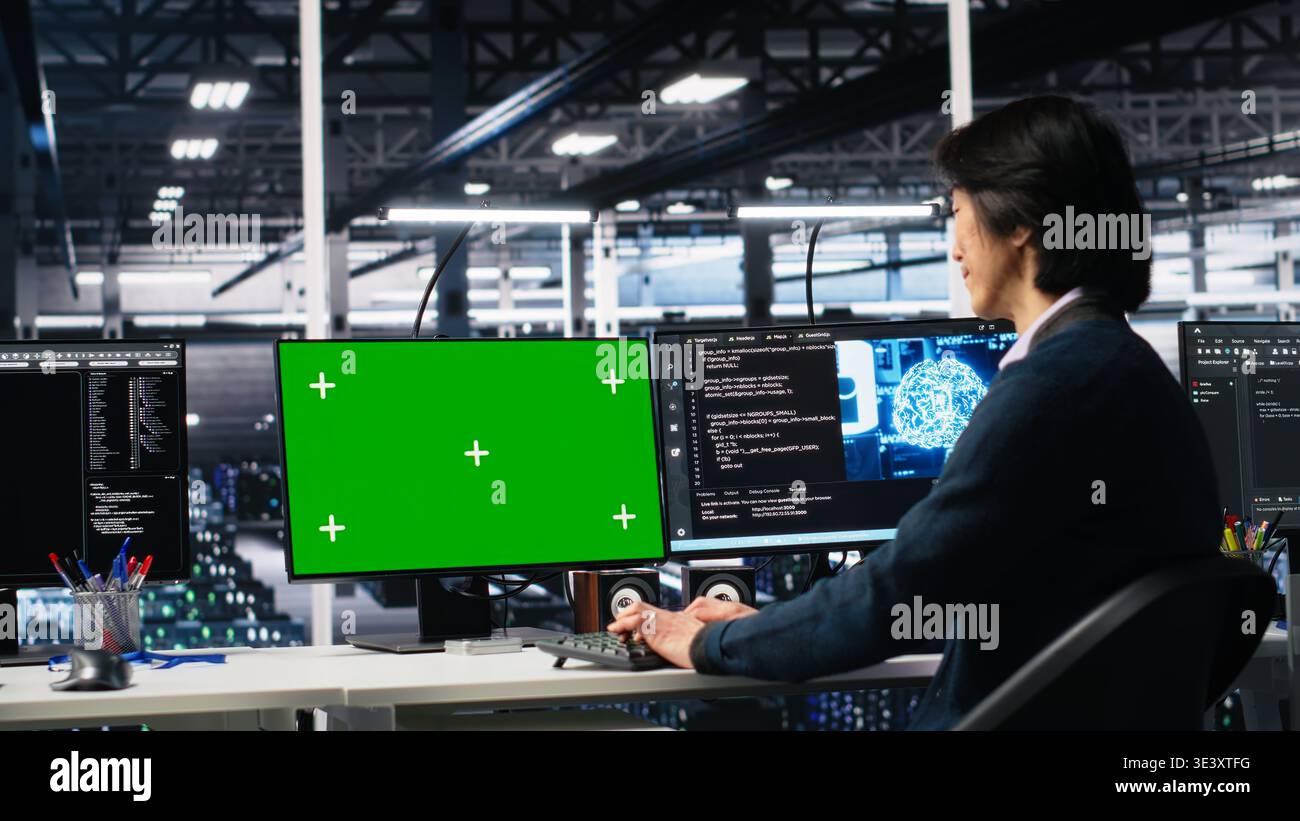 Data center technician managing AI systems using mockup PC. IT professional in tech startup office using artificial intelligence on green screen computer in server hub, camera A Stock Photo