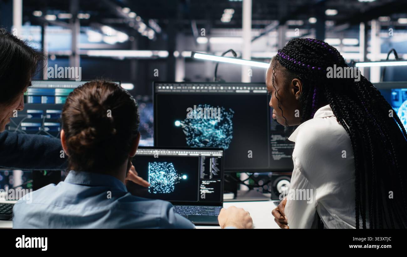 Teamworking data center technicians using machine learning algorithms to analyze large datasets. Server room colleagues gathered together at desk, collaborating, using AI neural networks, camera A Stock Photo