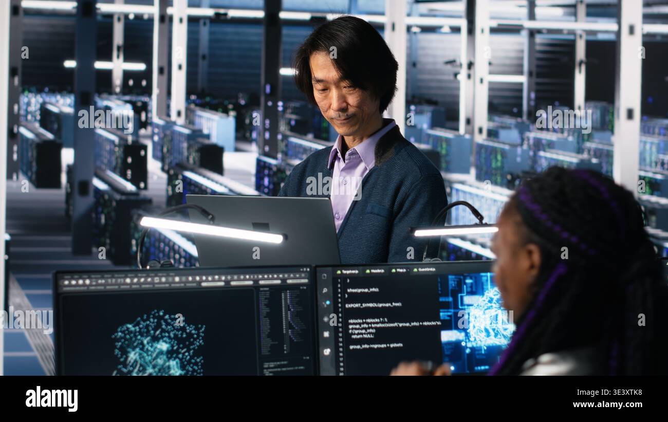 Software developers cooperating in data center, reviewing AI diagnostics on computer. IT staff members discussing in server room, optimizing machine learning systems, camera A Stock Photo