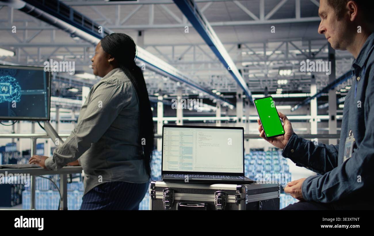 Server room software developer using mockup phone while waiting for updates to finish installing. Data center engineer uses green screen smartphone, waiting for code to finish compiling, camera A Stock Photo