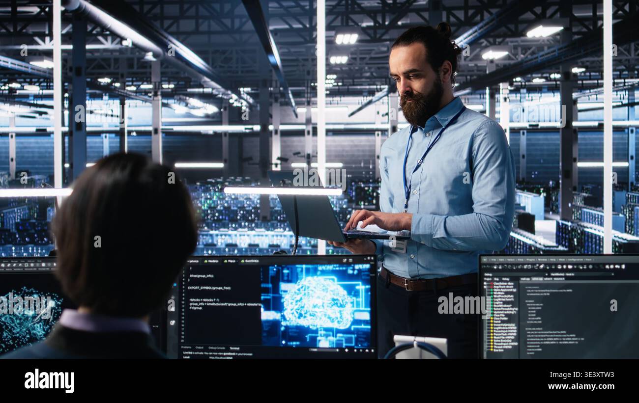 Manager supervising work of server room engineer using AI to review infrastructure diagnostics on devices. Tech company supervisor overseeing IT expert in data center analyzing data using AI, camera A Stock Photo