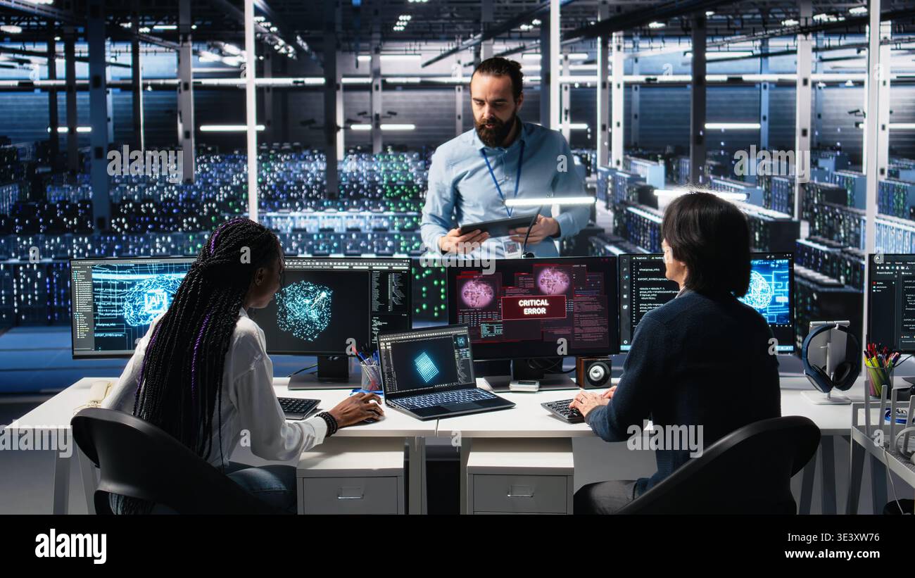 Data center manager coordinating programmers fixing critical error while using AI. Server room team leader overseeing workers repairing glitch popup while using artificial intelligence, camera A Stock Photo