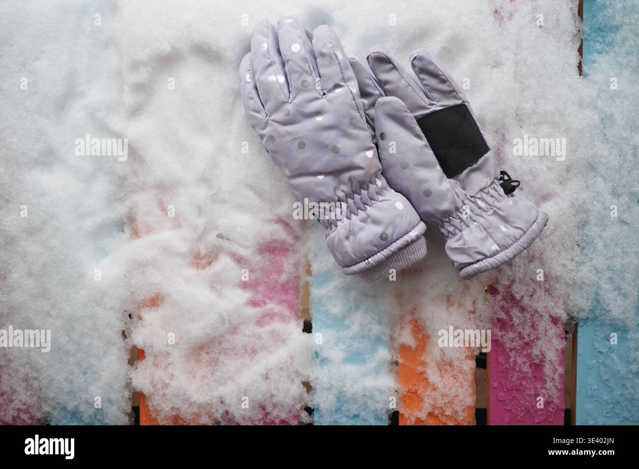 Warm gloves resting on colorful wooden surface in snow Stock Photo