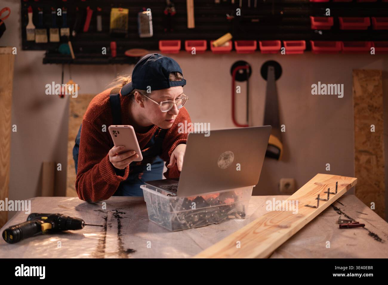 Carpenter Working In Woodwork Workshop Talking On Mobile Phone And Using Laptop Stock Photo
