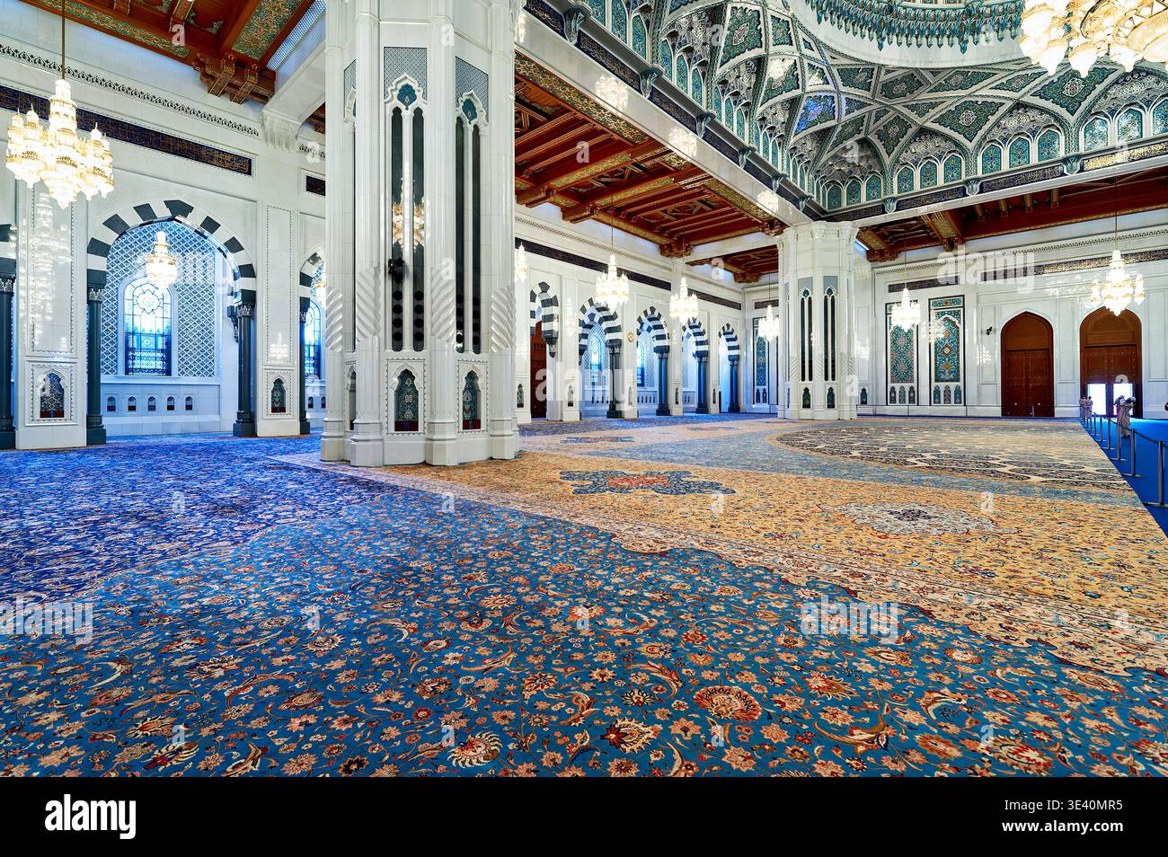 People walk inside Sultan Qaboos Grand Mosque in Muscat Oman. The space shows intricate designs and beautiful lights. Stock Photo