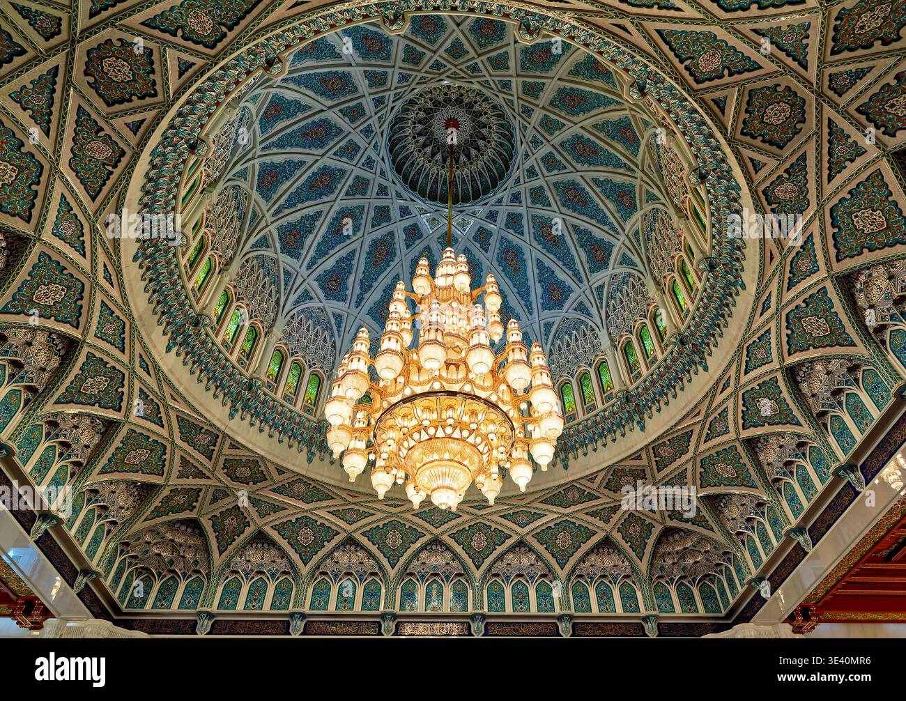 A large chandelier hangs from the ceiling inside Sultan Qaboos Grand Mosque in Muscat, Oman, showcasing intricate designs and details. Stock Photo