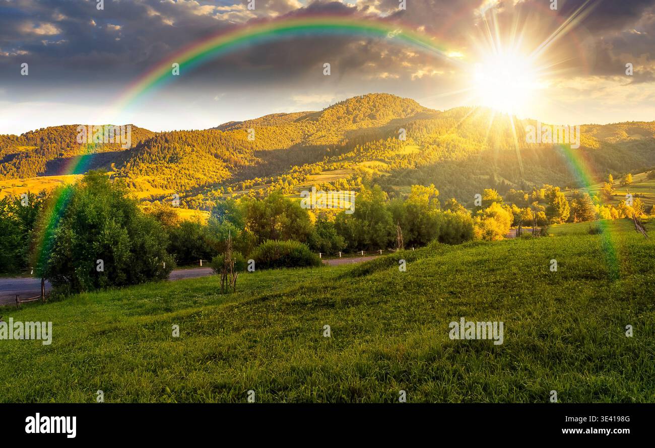 sunset over agricultural grassy field and rolling hills in mountainous rural scenery in summertime. wonderful countryside landscape in mountains with Stock Photo
