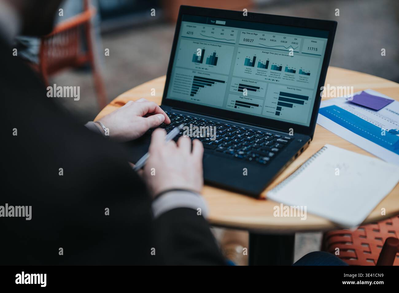 Business professional analyzing data dashboard on laptop at a cafe table while taking notes Stock Photo