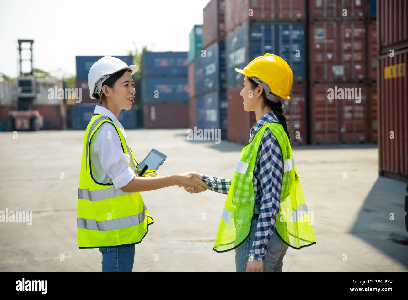 Two construction workers using tablet and clipboard at shipping container site Stock Photo