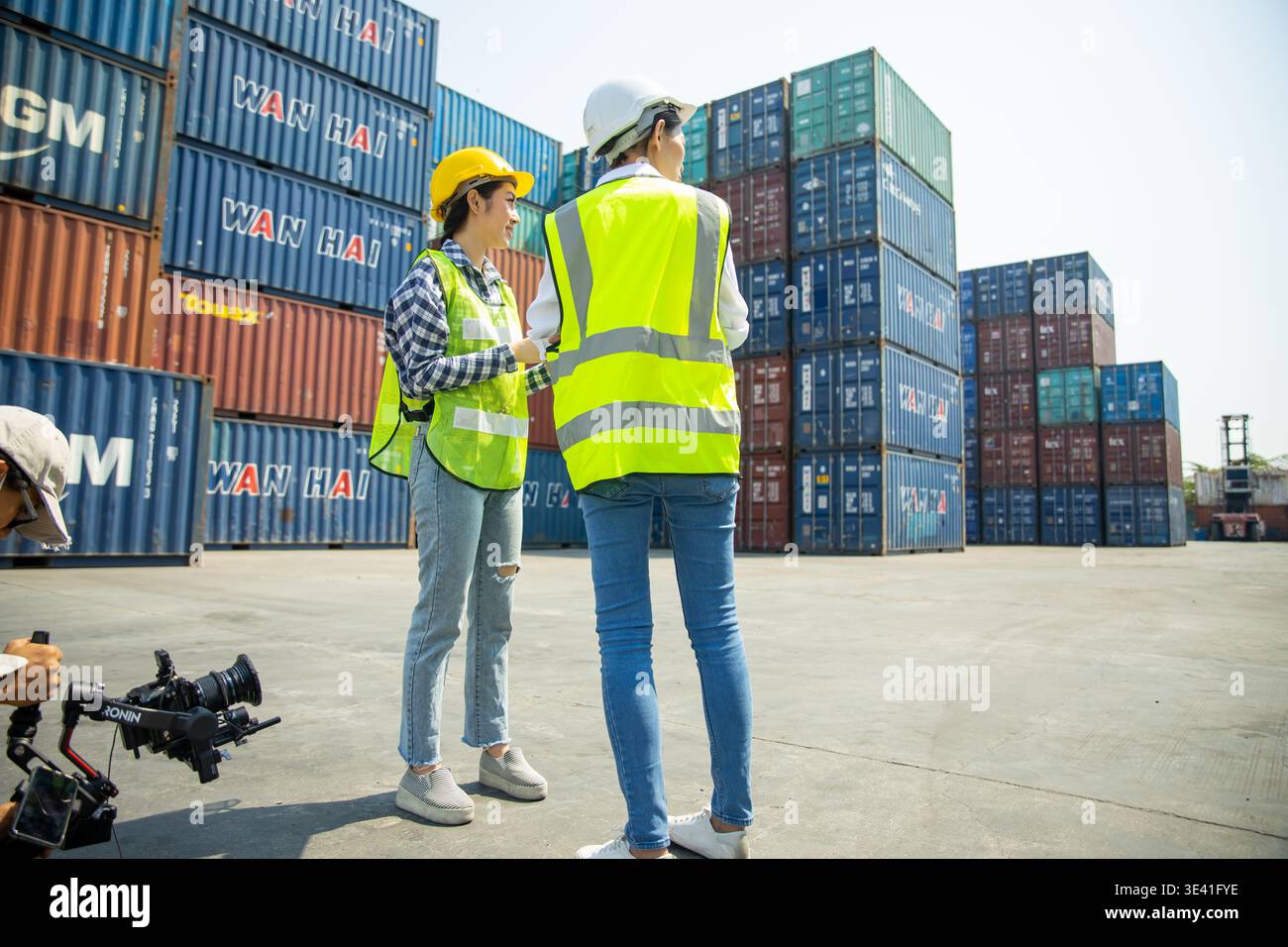 Two construction workers using tablet and clipboard at shipping container site Stock Photo