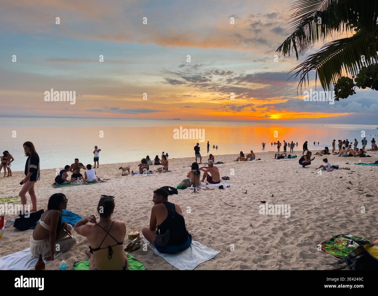People relaxing on white sand by a calm tropical sea whilst watching the sunset at Paliton Beach, Siquijor, Philippines. - Smartphone Captured Stock Image