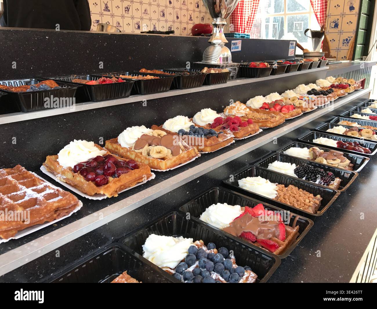 Waffles arranged in neat rows, each one decorated with a different topping. Variations include fresh fruits, chocolate, and whipped cream. Stock Photo