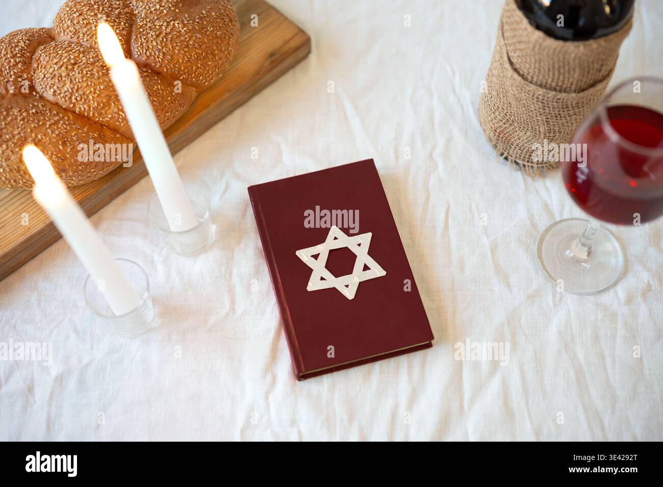 Shabbat Shalom concept. Challah bread, red kosher wine, book and candles on table. Traditional Jewish Shabbat kiddush ritual. Stock Photo